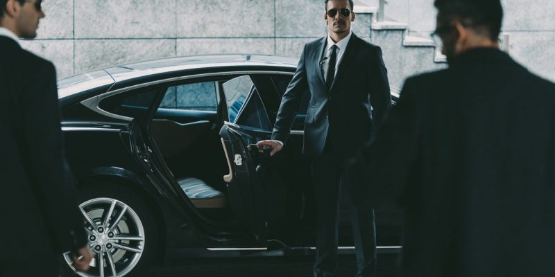 bodyguard-in-sunglasses-opening-car-door-to-businessman.jpg